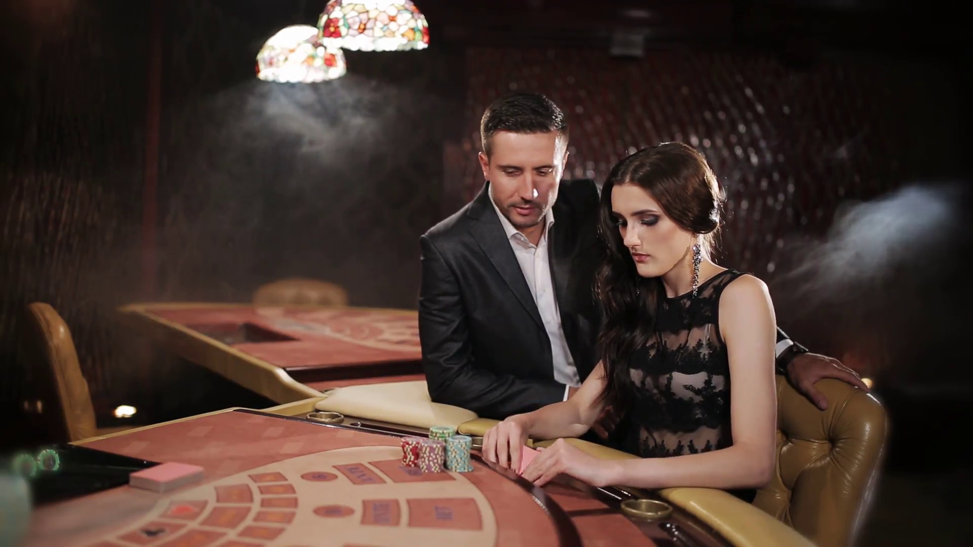 Симпатичная шатенка в вечернем платье и ее эллегантный спутник играют в покер в престижном казино