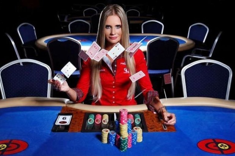 Девушка крупье в строгом костюме перебрасывает карты, сидя за игорным столом