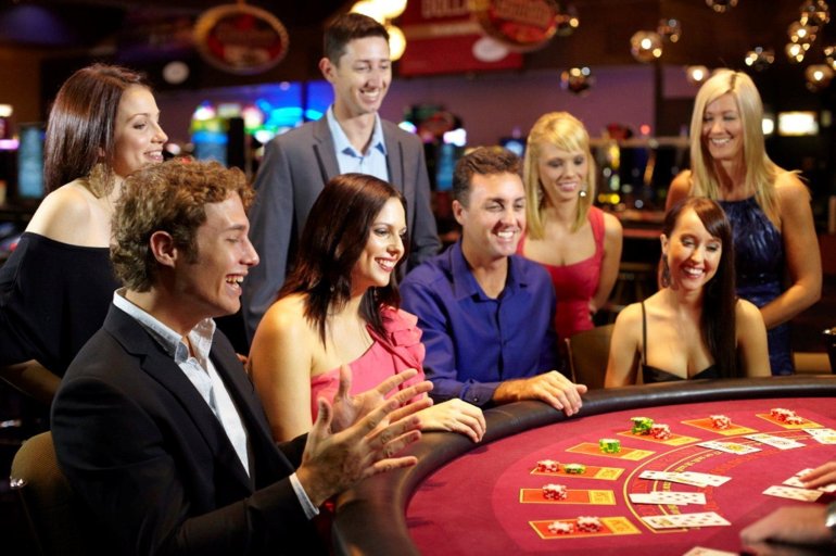 Молодые мужчины и красивые девушки в вечерених платьях веселятся в дорогом казино за игрой в блэкджек
