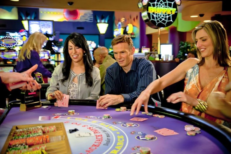 Мужчина играет в блэкджек в казино в компнаии двух женщин - блондинки и брюнетки