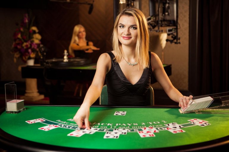 Приветливая девушка крупье с красивыми белыми волосами ведет игру в блэкджек в зале казино