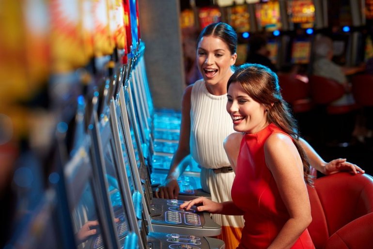 Красивые молодые женщины в вечерних платьях играют в автоматы в зале престижного казино