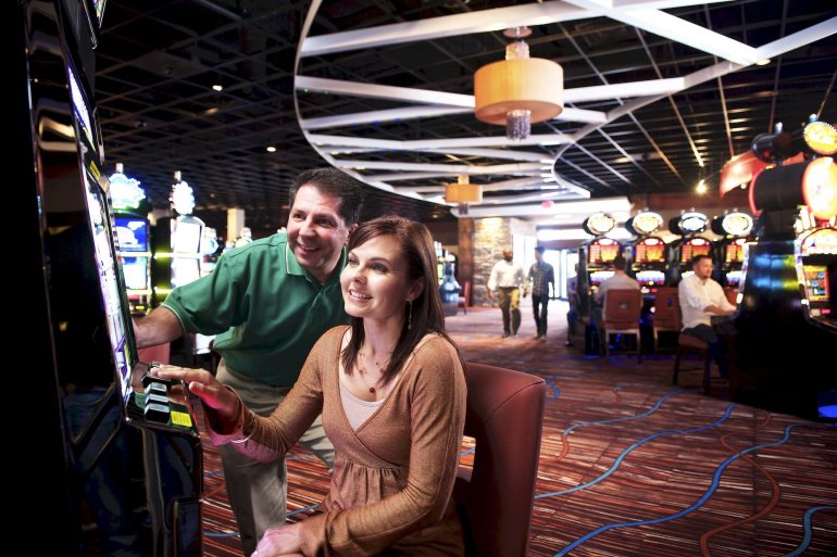 Мужчина и женщина зрелого возраста играют на автомате в просторном зале казино