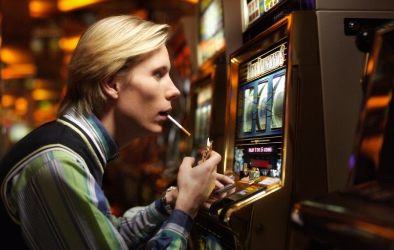 обескураженый блондин с сигаретой во рту не может поверить, что на игровом автомате у него выпали три семерки