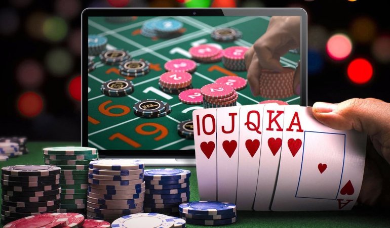 На мониторе планшета открыт сайт онлайн казино, а рядом игрок держит в руке карты чирвовой масти