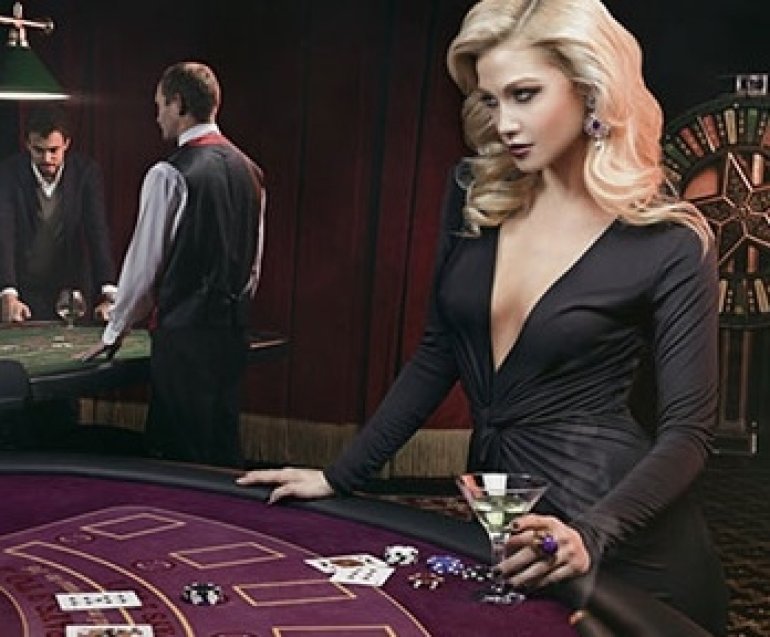 Сексуальная блондинка с откровенным декольте стоит с бокалом алкоголя за игорным столом