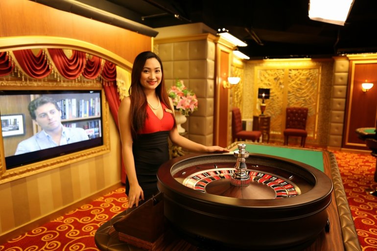 Миниатюрная азиатка крупье позирует у колеса рулетки в зале казино