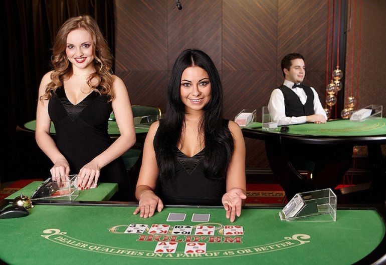 Две красотки крупье в черных платьях сидят за столом для холдем покера