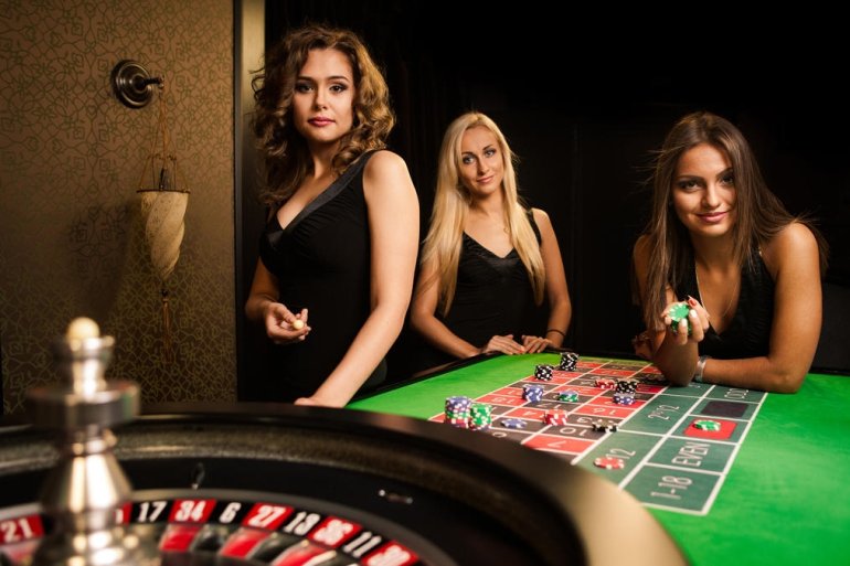 Три красотки крупье в ожидании игроков у стола для рулетки в зале роскошного казино