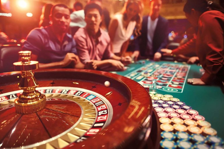 Колесо рулетки вращается, а на заднем фоне сидят азартные игроки, болеющие за свои ставки