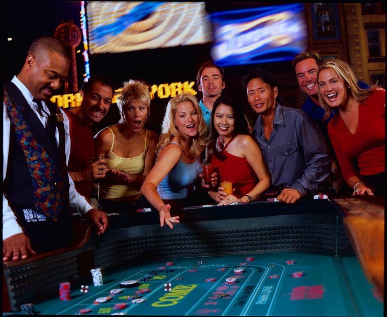 Крупье обслуживает стол для крэпса, а несколько азартных игроков окружили его и ждут исхода игры