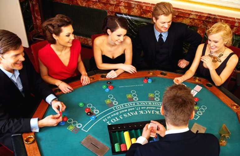 Мужчины в строгих костюмах и женщины в вечерних платьях за игрой в блэкджек в казино ВИП-уровня
