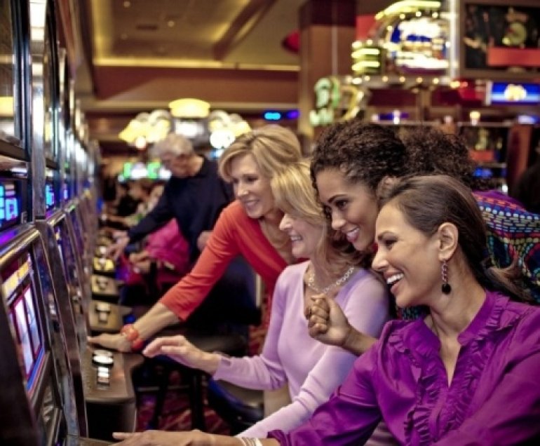Молодые красивые женщины говорят и смеются за игрой на автоматах в казино