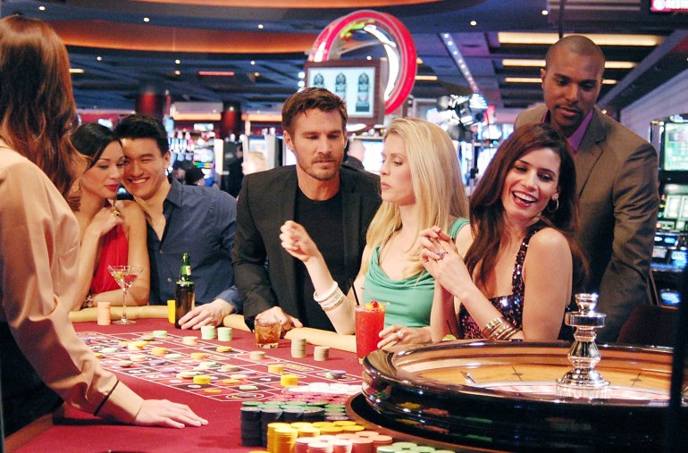 Богатые мужчины и красивые женщины веселятся за игрой в рулетку в зале престижного казино