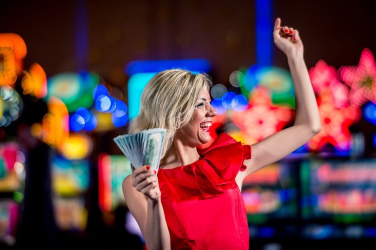 Блондинка радуется своему выигрышу в казино, размахивая пачкой денег