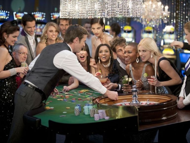 Элитная компания за игрой в рулетку с симпатичным молодым крупье в шикарном казино